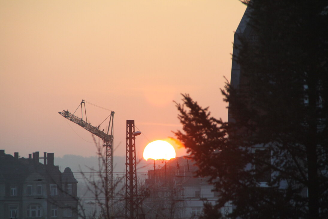 Schimmriger Sonnenaufgrang vor Stadtkulisse mit Baukran